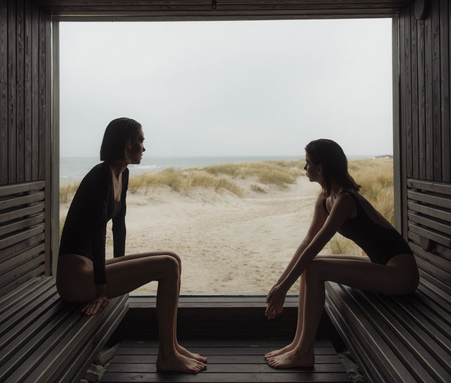 Two people seated in a sauna looking out to the water